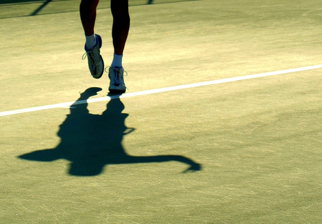 テニスコートに立つ男性とその影
